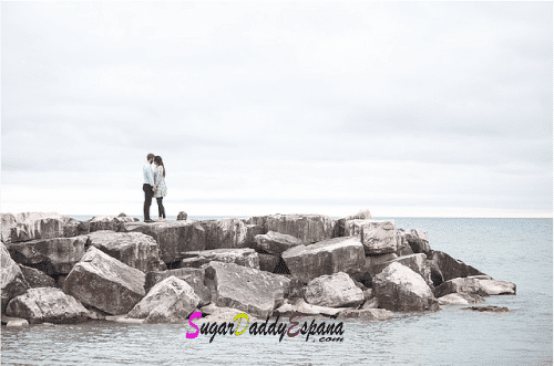 Chica y chicos de lejos abrazados en las rocas del mar